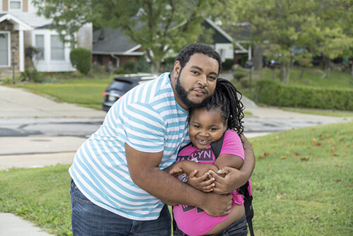 Father and daughter hugging outdoors on front lawn