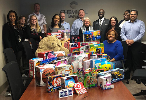 A conference table full of unwrapped donated toys with a group of employees standing behind them.