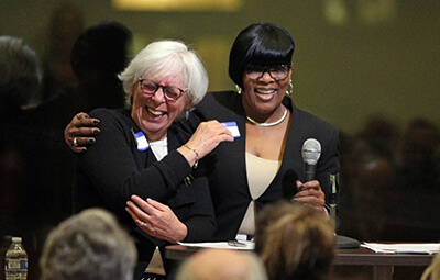 Two women at podium with arms around each other smiling