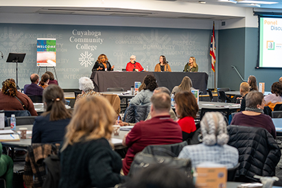 4 panelists on stage with attendants sitting in chairs listening