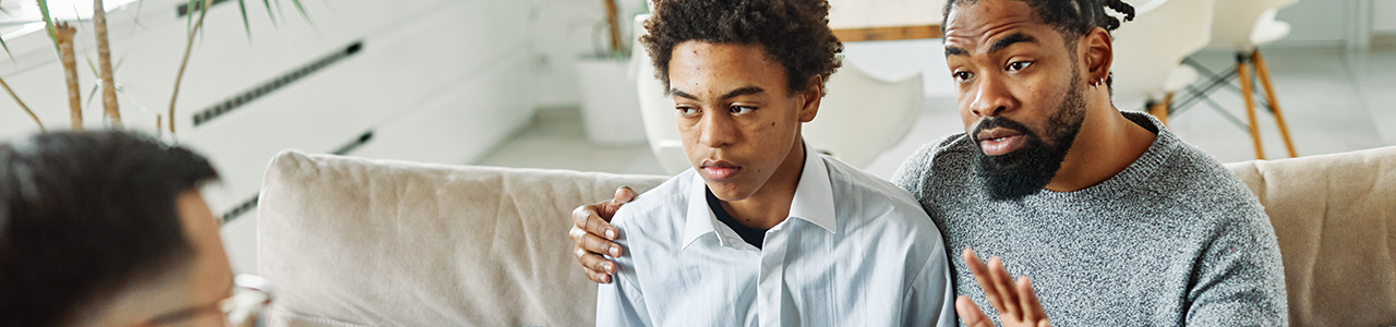 Father and son sitting on couch with fathers are around son.