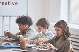 Group of schoolchildren sitting in row and making wooden models.