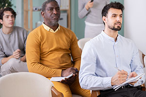 Men of different ages listen attentively to teacher and take notes in notebooks during a lecture at the learning center.