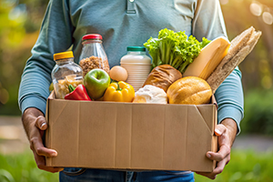 Cropped image of a person holding a cardboard box full of groceries.