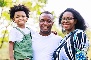 Smiling parents and son together while standing in the park in the daytime in summer.