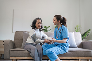SkilledCareNurse Caregiver measuring blood pressure of senior woman on sofa in home.
