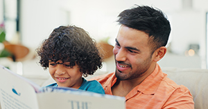 SupportedVisits Father, boy and reading book on sofa, smile and learning with storytelling, development and literature.