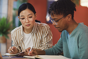 Young woman helping a young man study at a table.